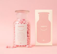 a jar filled with pink candies next to a white box on a pink background