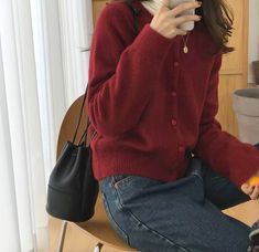 a woman sitting on top of a wooden chair holding a cell phone