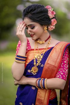 a woman in a blue and orange sari with jewelry on her neck, holding her hand to her face