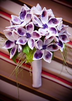 a white vase filled with purple flowers sitting on top of a window sill next to a red and white striped wall