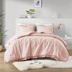 a bed with pink comforter and pillows in a room next to a potted plant