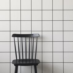 a black chair sitting in front of a white tiled wall with a wooden seat on it