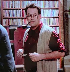 a man standing in front of a bookshelf with a pipe in his mouth