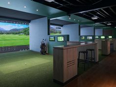 an indoor golf simulator with green grass and bar stools in front of the television