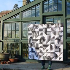 a person holding up a quilt in front of a green building with large glass windows