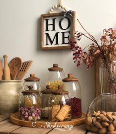 a wooden table topped with glass jars filled with different types of food next to a sign that says home