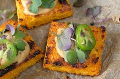 four square pieces of food with vegetables on them sitting on wax paper and placed on top of each other