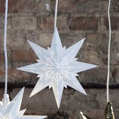 three white paper stars hanging from strings in front of a brick wall, with one star lit up