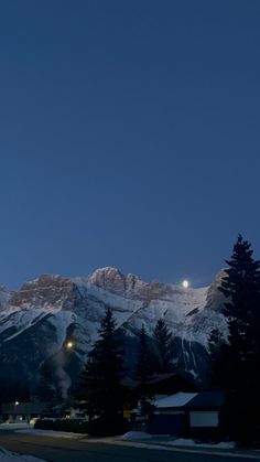 the mountains are covered in snow and lit up by street lights at night with full moon