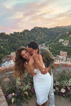 a man and woman embracing each other on top of a hill with flowers in the foreground