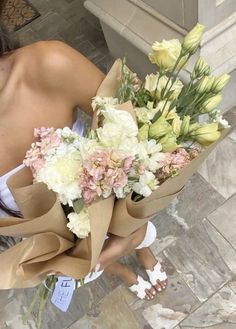 a woman holding a bunch of flowers on top of a stone floor next to a building