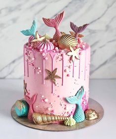 a pink cake with gold decorations on top and under the icing mermaid tailes