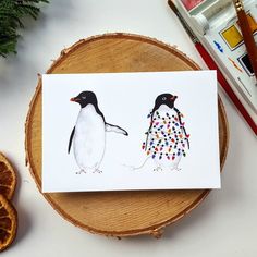 two penguins are standing next to each other on a piece of wood with paintbrushes