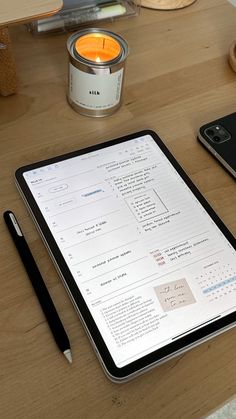 a tablet computer sitting on top of a wooden table next to a cell phone and pen