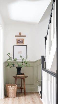 a plant in a black vase sitting on top of a wooden table next to a stair case