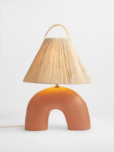 an orange table lamp sitting on top of a wooden base with a beige shade over it