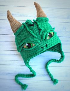 a crocheted green hat with horns and eyes on top of a wooden table