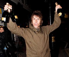 a man holding two bottles of wine in his hands while standing on the street at night