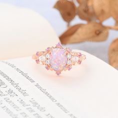 an opal and diamond ring sitting on top of a book with leaves in the background