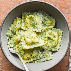 a bowl filled with broccoli and cheese on top of a wooden table next to a fork