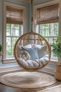 a hanging chair in front of two windows with pillows on it and a potted plant next to the window