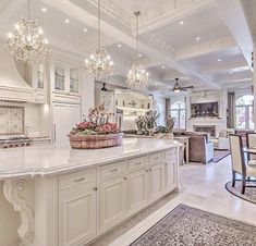 a large white kitchen with chandeliers hanging from the ceiling and marble counter tops