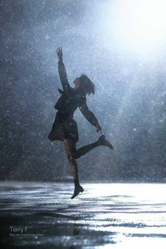 a woman is jumping in the air on a rainy day with her arms up and legs spread out