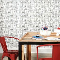 two red chairs sitting at a wooden table in front of a wallpapered room