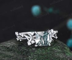 a silver ring sitting on top of a mossy green rock in front of a black background