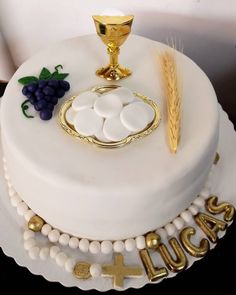 a cake decorated with white frosting and gold decorations on a table next to a cross