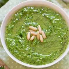 a white bowl filled with green pesto and almonds on top of a table