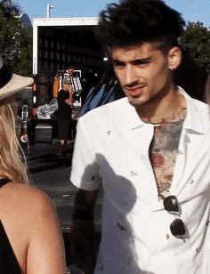 a man in a white shirt and tie standing next to a woman with tattoos on her chest