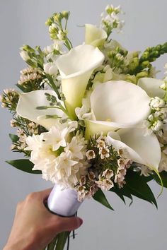 a bouquet of white flowers is held by a person's hand in front of a gray wall