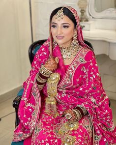 a woman in a pink bridal outfit sitting on a chair with her hands together