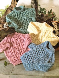 knitted sweaters in various colors and sizes on the floor next to a potted plant