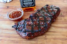 a piece of steak sitting on top of a wooden cutting board next to a bottle of whiskey