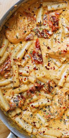 a skillet filled with pasta and meat covered in sauce on top of a wooden table