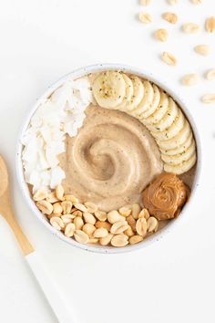 a bowl filled with nuts and peanut butter next to a wooden spoon on a white surface