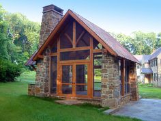 a small stone building with a brick chimney and glass doors on the front door is surrounded by lush green grass