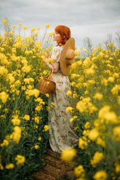 a woman is standing in a field with yellow flowers and holding a wicker basket