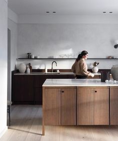 a woman standing at the kitchen counter in front of an island with two vases on it