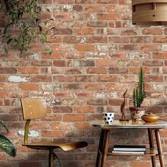 two chairs and a table in front of a brick wall with potted plants on it