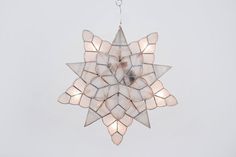 a star shaped chandelier hanging from a chain on a gray background with white lights