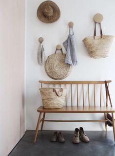 three baskets hanging on the wall next to a bench with two hats and one bag