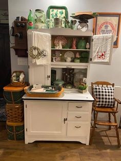 an old fashioned kitchen with white cabinets and wooden chairs in front of the cupboards