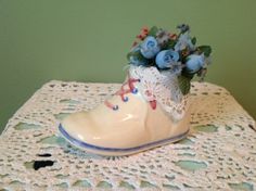 a white boot with blue flowers in it sitting on a doily covered tablecloth