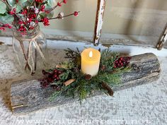 a candle is sitting on a piece of wood next to a vase with red berries and greenery