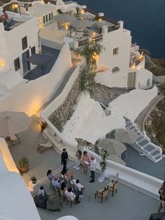 an aerial view of people sitting at tables in front of white buildings with lights on them