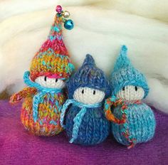 three crocheted gnomes sitting next to each other on a purple tablecloth