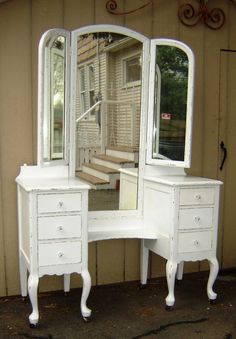 a white vanity with mirror and drawers in front of a house